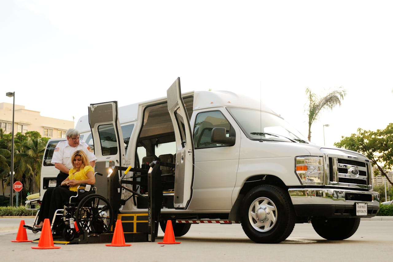 A transportation van with a wheelchair user and assistant using the ramp outdoors, ensuring accessibility.